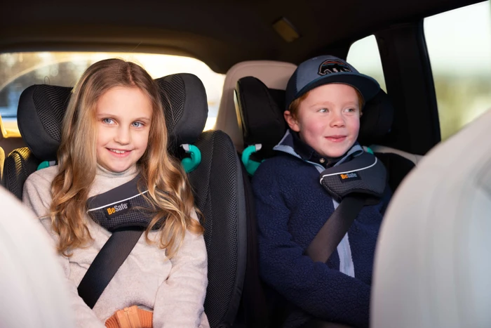 Två barn sitter bredvid varandra i BeSafe-bältesstolar i en bil, med PAD+ synligt på axelbältena