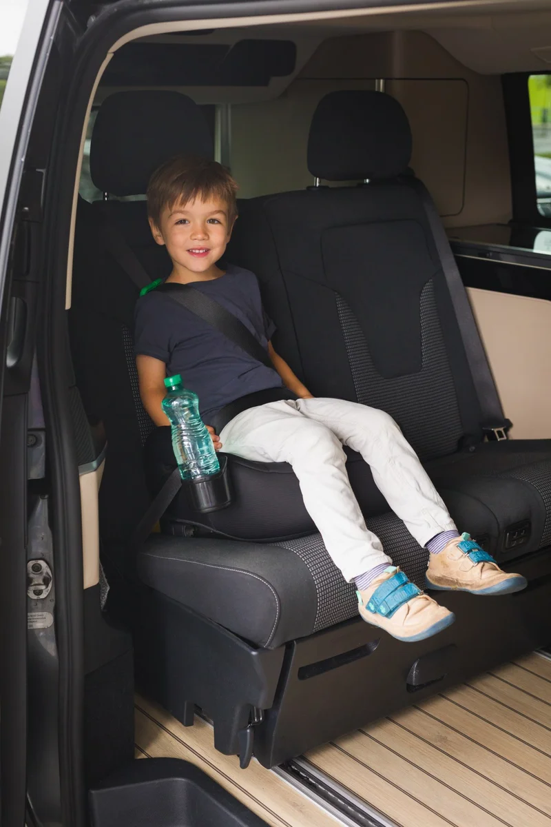 Barn sitter i Fillikid I-Size bälteskudde i en bil, med bilbälte korrekt placerat och flaskhållare i användning