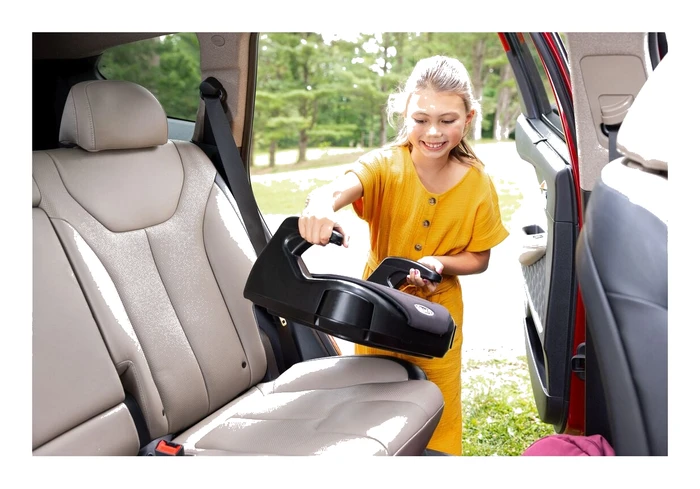 Flicka bär Graco Booster Basic i ena handen på väg till bilen, visar kuddens låga vikt